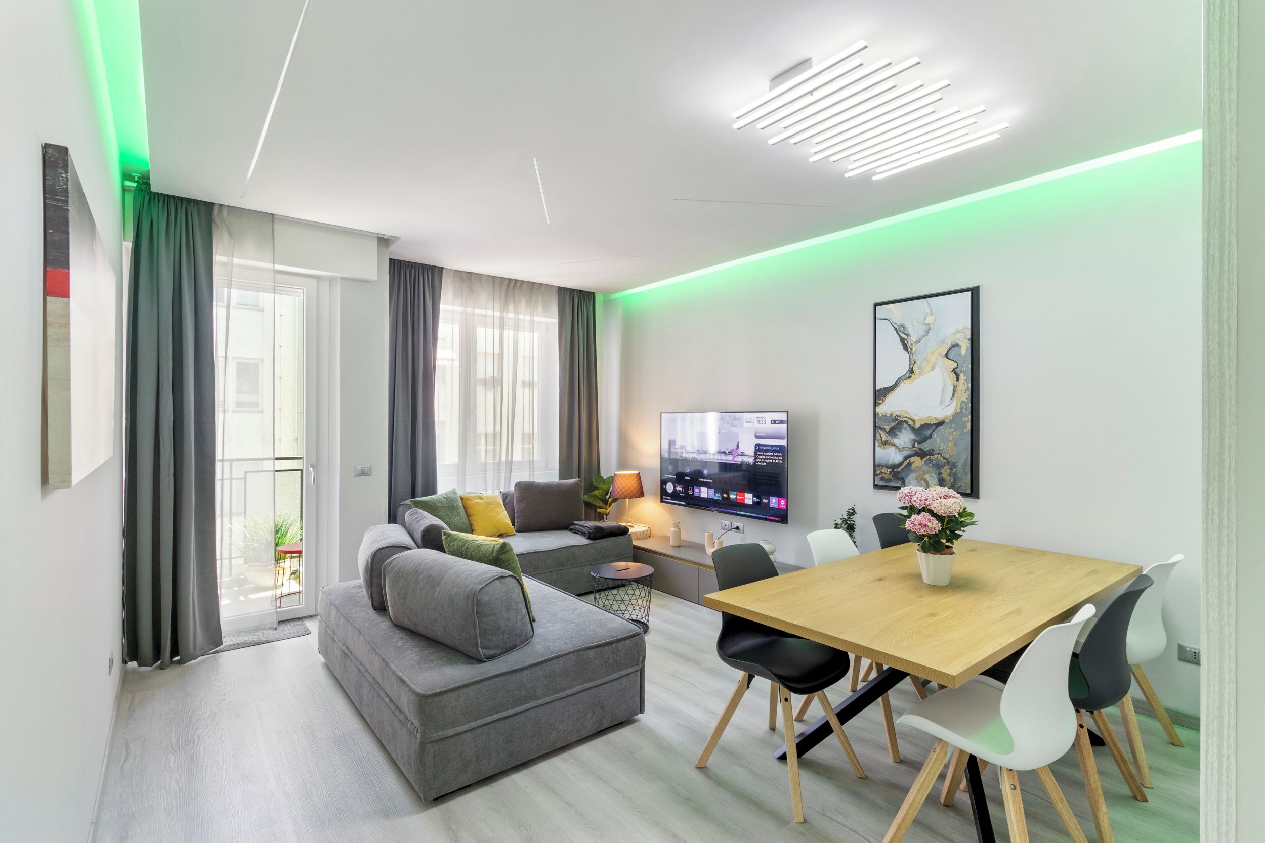 A modern living room with a grey sofa, a wooden dining table, and a flat-screen TV.