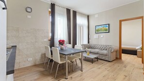 A dining area with a table, chairs, and a sofa. There is a clock on the wall and a painting above the sofa. - Love Story - inclusa ricca colazione a buffet (Cormons)