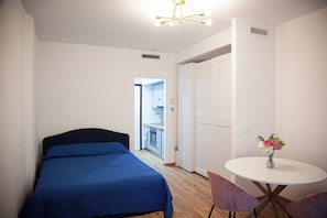 Ein Schlafzimmer mit einem Bett, einem runden Tisch mit Stühlen, einer weißen Tür und einer Deckenleuchte.