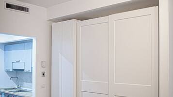 Una habitación con un armario blanco grande, una cocina con muebles bajos y un lavabo, y una lámpara en el techo.