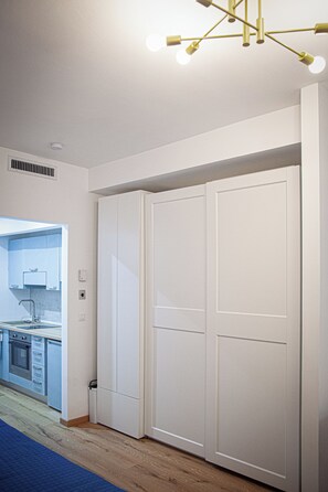 Una habitación con un armario blanco grande, una cocina con muebles bajos y un lavabo, y una lámpara en el techo.