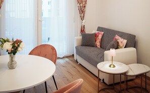 Una sala de estar con un sofá, dos mesas auxiliares, una mesita redonda y un jarrón con flores.