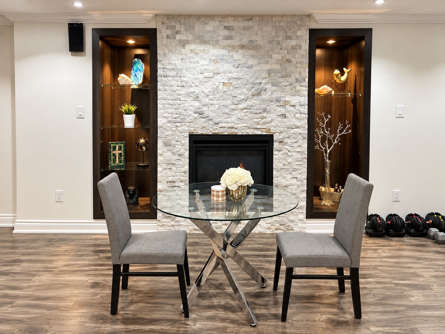 A dining area with a glass table and two chairs, a stone fireplace, and a shelf with decorative items.