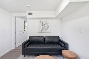 Ein modernes Wohnzimmer mit einem schwarzen Ledersofa, einem hölzernen Hocker und einem motivierenden Wandbild.