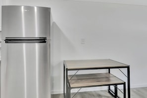 Un réfrigérateur en acier inoxydable se trouve à côté d’une table en bois simple, dotée de pieds en métal.