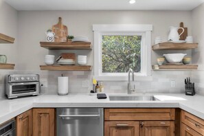 A modern kitchen with a built-in oven, a stainless steel dishwasher, wooden cabinets, and a window with a view of trees. - Treehouse on Daly | Steps to Main St & Trolley (Park City)