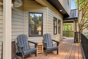 A covered porch with two Adirondack chairs, a small table, and a view of trees through a window. - Treehouse on Daly | Steps to Main St & Trolley (Park City)