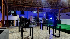 An outdoor seating area with thatched roof, tables, chairs, and a green artificial turf. - Margot (Playa del Carmen)