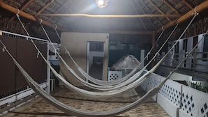 A hammock suspended between two white railings in a covered outdoor area with a tiled floor and a thatched roof. - Margot (Playa del Carmen)
