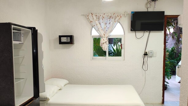 A single bed with a white mattress and pillows, a ceiling fan, a television mounted on the wall, and a window with curtains. - Margot (Playa del Carmen)