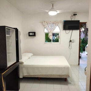 A single bed with a white mattress and pillows, a ceiling fan, a television mounted on the wall, and a window with curtains. - Margot (Playa del Carmen)