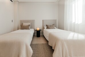 Camera d'albergo con due letti singoli, un tavolino con una lampada e vista sull'esterno attraverso una finestra.