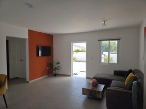 Ein Wohnzimmer mit einer Couch, einem Couchtisch, einem an der Wand montierten Fernseher und einer Tür zu einem Außenbereich.