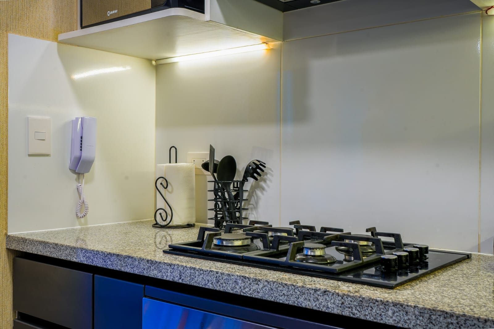 A kitchen with a gas stove, a telephone, and a paper towel holder.