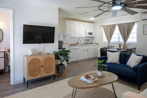A modern living room with a blue sofa, a coffee table with books, a TV, and a ceiling fan. - Tide · Beach days, family nights (Cocoa Beach)