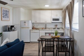 A compact kitchen with white cabinets, a microwave, and a dishwasher. There is a dining table with chairs, a coffee machine, and a potted plant. - Tide · Beach days, family nights (Cocoa Beach)