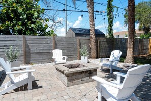 An outdoor patio with white Adirondack chairs, a fire pit, and a wooden fence. - Tide · Beach days, family nights (Cocoa Beach)