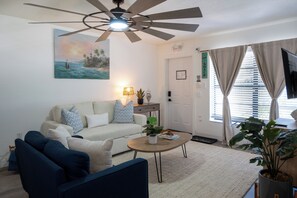 A living room with a ceiling fan, a painting, a sofa, a coffee table, and a TV. - Tide · Beach days, family nights (Cocoa Beach)