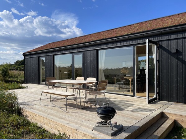 A modern building with a deck, outdoor seating, and a barbecue grill. - Lovely holiday home on the Røsnæs coast (Kalundborg)