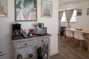 A kitchenette with a coffee maker, a kettle, and a food processor. There is a dining area with a table and chairs. - Sunset · Beach days together | 2BR, sleeps 6 (Cocoa Beach)