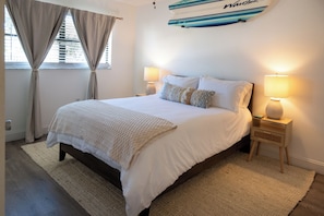 Ein Schlafzimmer mit einem großen Bett, zwei Nachttischlampen, einem Teppich und einer Surfbrett-Dekoration an der Wand.
