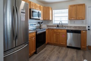 A modern kitchen with stainless steel appliances, wooden cabinets, and a granite countertop. - Sunset · Beach days together | 2BR, sleeps 6 (Cocoa Beach)
