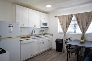 A compact kitchen with white cabinets, a microwave, a sink, and a dining area with a table and chairs. - Coral House · Whole House · 3 Suites · Sleeps 12 (Cocoa Beach)