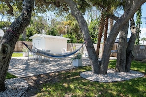 A hammock between trees, a shed, and a patio area with chairs and a table. - Coral House · Whole House · 3 Suites · Sleeps 12 (Cocoa Beach)