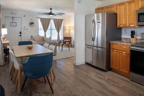 A modern kitchen with a stainless steel refrigerator, wooden cabinets, and a dining area with blue chairs. - Coral House · Whole House · 3 Suites · Sleeps 12 (Cocoa Beach)
