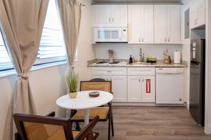 Eine kleine Küche mit weißen Schränken, einer Mikrowelle, einem Kühlschrank und einem Essbereich mit Tisch und Stühlen.