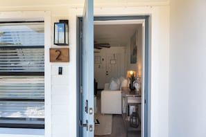 A doorway leading into a room with a white door, a number '2' sign, and a small table with a lamp and decorative items. - Garnet Beaches · 2 Houses · 6 Suites · Sleeps 24 (Cocoa Beach)