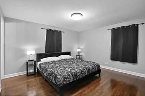 A bedroom with a bed, two bedside tables, a nightstand, a ceiling light, and two windows with curtains. - Stylish and spacious 4-bedroom 2.5-bathroom home in Schaumburg (Schaumburg)