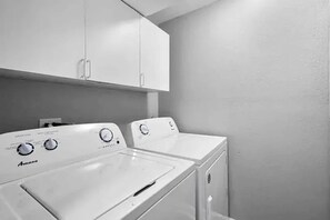 A laundry area with two white front-loading washing machines and a cabinet above them. - Stylish and spacious 4-bedroom 2.5-bathroom home in Schaumburg (Schaumburg)