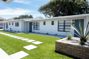 A modern two-story house with a well-maintained lawn and a brick planter with a large plant. - Sand · Pack light, stay awhile | 2BR + laundry (Cocoa Beach)