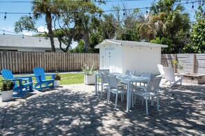 A patio with a white table and chairs, a shed, and a wooden fence. - Palm House · Whole House · 3 Suites · Sleeps 12 (Cocoa Beach)