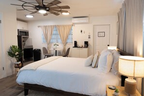 A hotel room with a bed, bedside lamp, ceiling fan, and a small table with a plant. - Palm House · Whole House · 3 Suites · Sleeps 12 (Cocoa Beach)