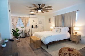 Ein Hotelzimmer mit einem Bett, Nachttischen, einem Schreibtisch, einem Sessel, einem Deckenventilator und einem Fenster mit Vorhängen.