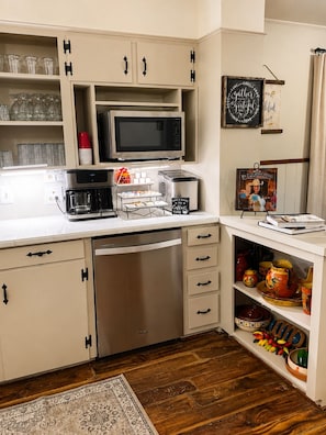 A kitchen with a microwave, coffee maker, toaster, and a coffee station.