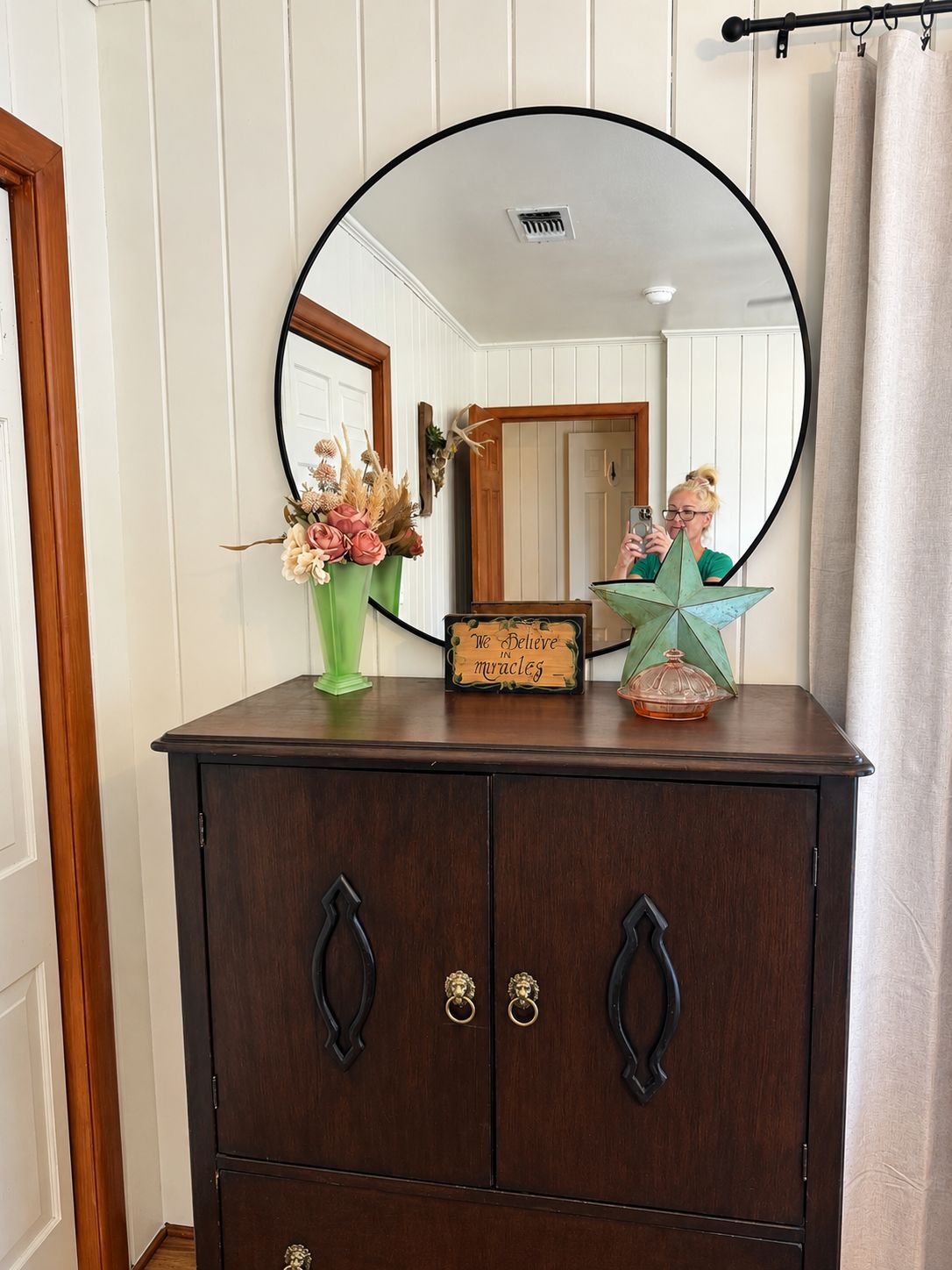 A wooden dresser with a large mirror, a vase with dried flowers, and a star-shaped object on top.