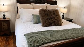 Una cama bien hecha con cabecera de madera, dos mesitas de noche con lámparas y una ventana con cortinas.