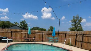 Una piscina con recinzione in legno, una rete da pallavolo e una ghirlanda di luci.