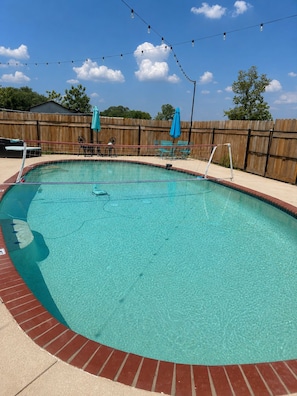 A swimming pool with a wooden fence, a volleyball net, and a string of lights.