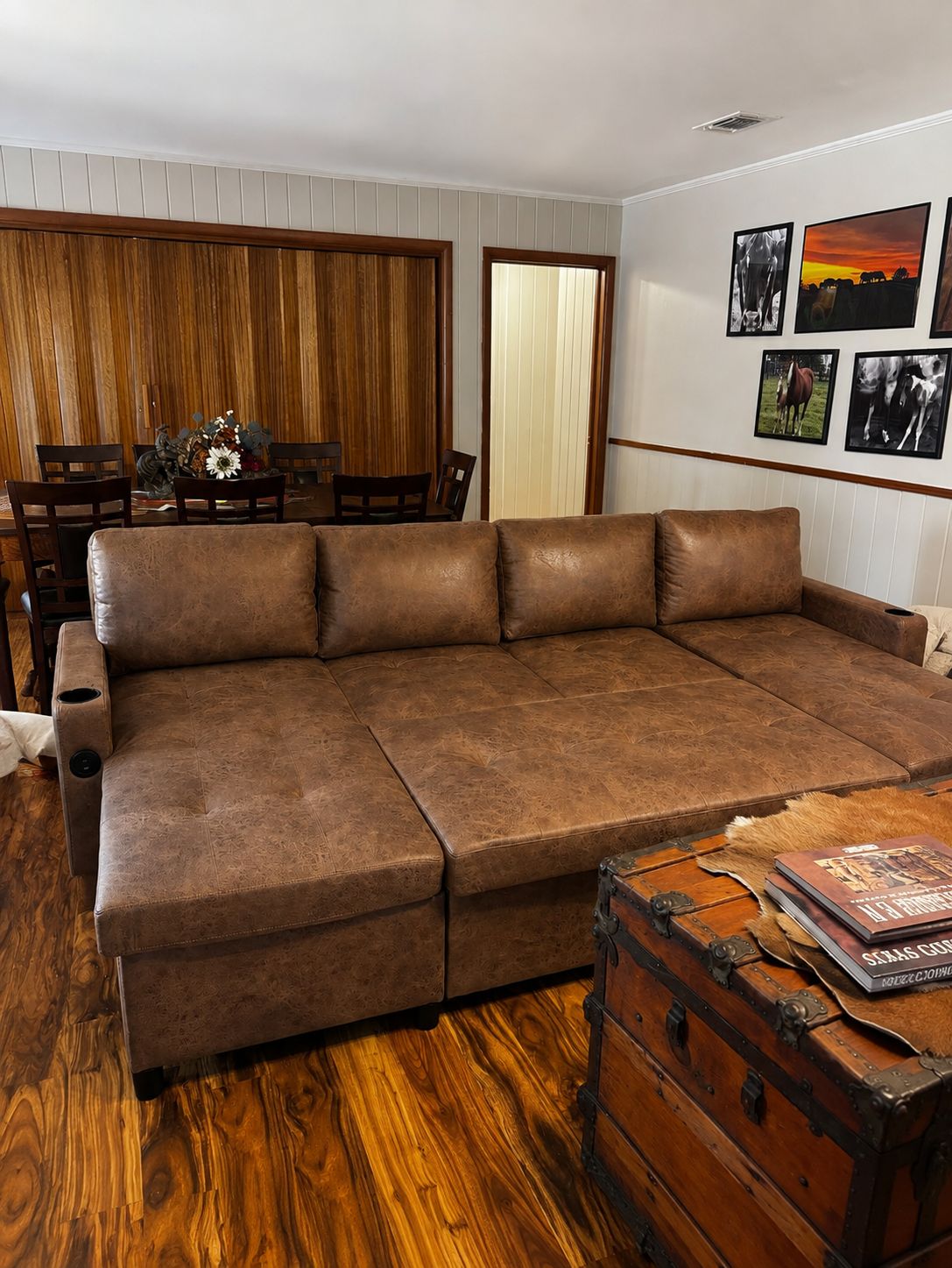 Ein Ecksofa in einem Raum mit Holzvertäfelung, einem Esstisch mit Stühlen und einer Wand mit gerahmten Bildern.
