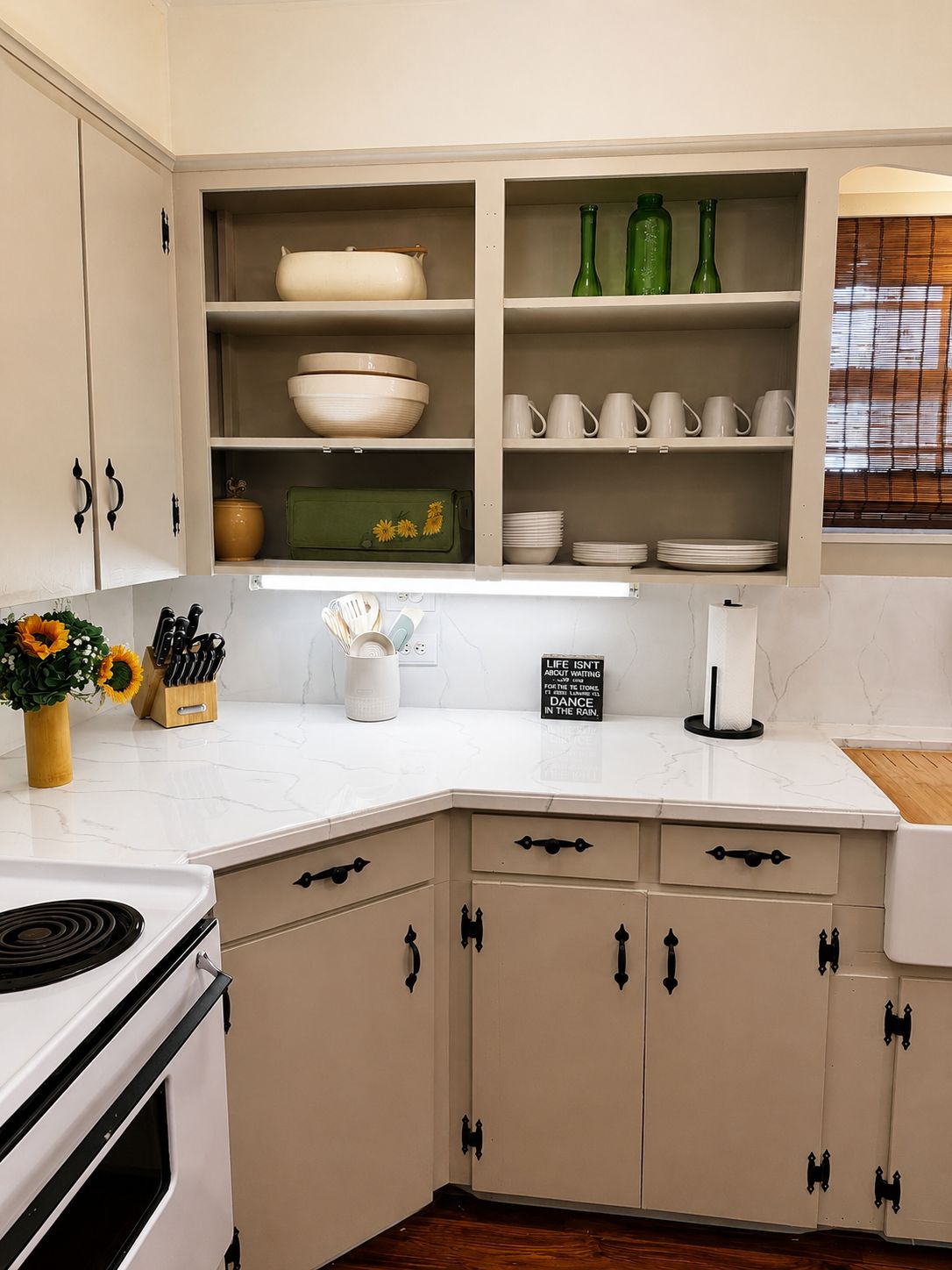 Una cocina con armarios blancos, una estufa y una encimera con un jarrón de girasoles.