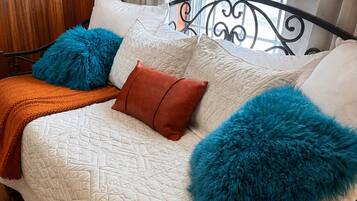Cama com cobertura branca acolchoada, manta marrom e duas almofadas azuis fofas.