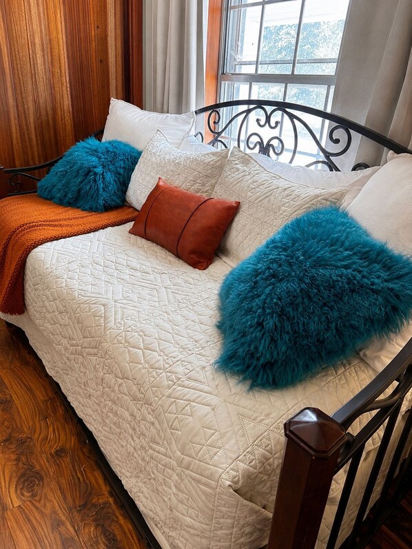A bed with a quilted white cover, a brown throw blanket, and two blue fluffy pillows.