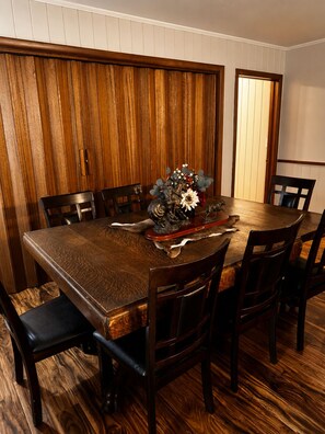 A dining room with a wooden table surrounded by chairs, a vase with flowers, and a wooden panel wall.