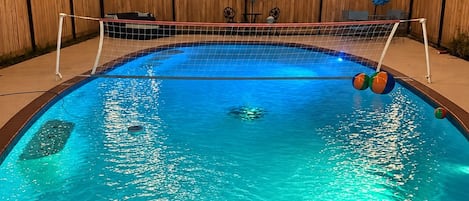 A swimming pool with a 4 ft depth marker, surrounded by a wooden fence, and string lights overhead.