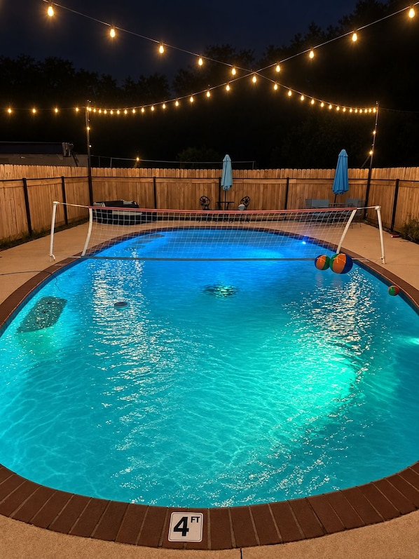 A swimming pool with a 4 ft depth marker, surrounded by a wooden fence, and string lights overhead.