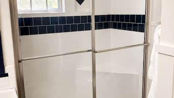 A bathroom with a glass-enclosed shower, white tiles, and a wooden floor.